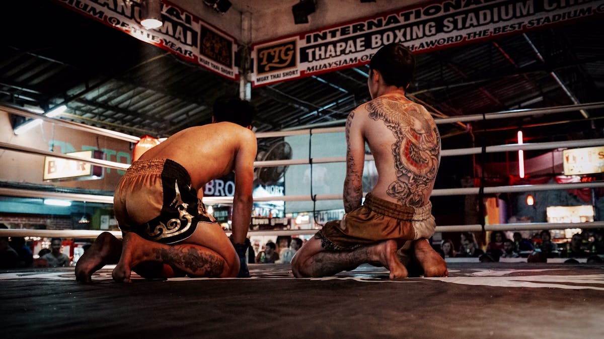 Tattooed Muay Thai fighters kneeling at Thapae Boxing Stadium, Thailand